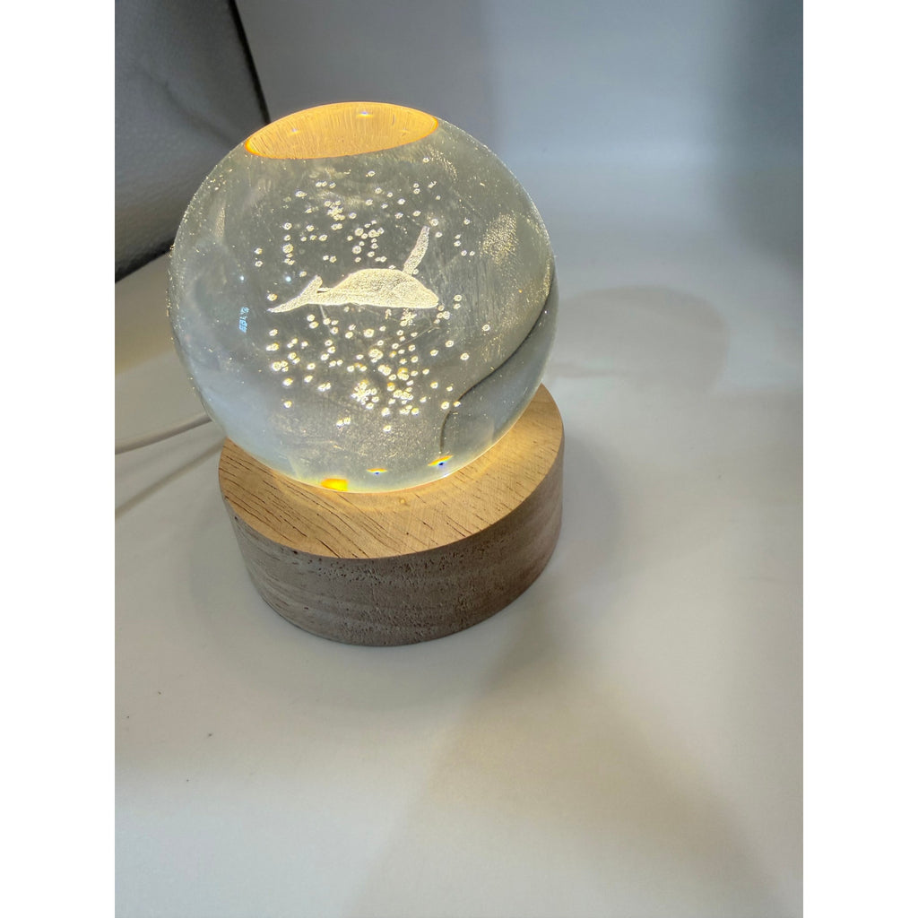 Laser etched crystal ball with blue whale design on LED stand, showcasing detailed whale engraving and vibrant blue illumination.