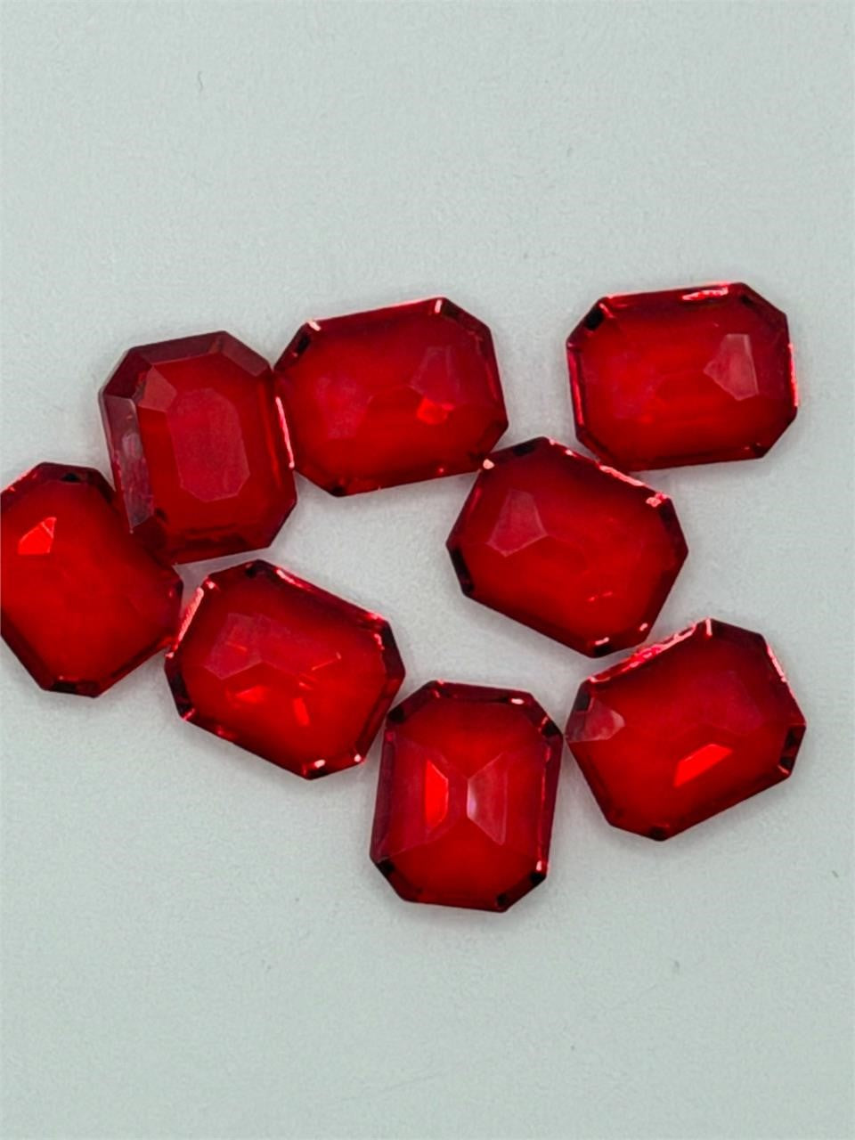 Seven red faceted emerald cut gemstones, 9x10mm, showcasing their vibrant color and sparkling facets, from Republic Mercantile.