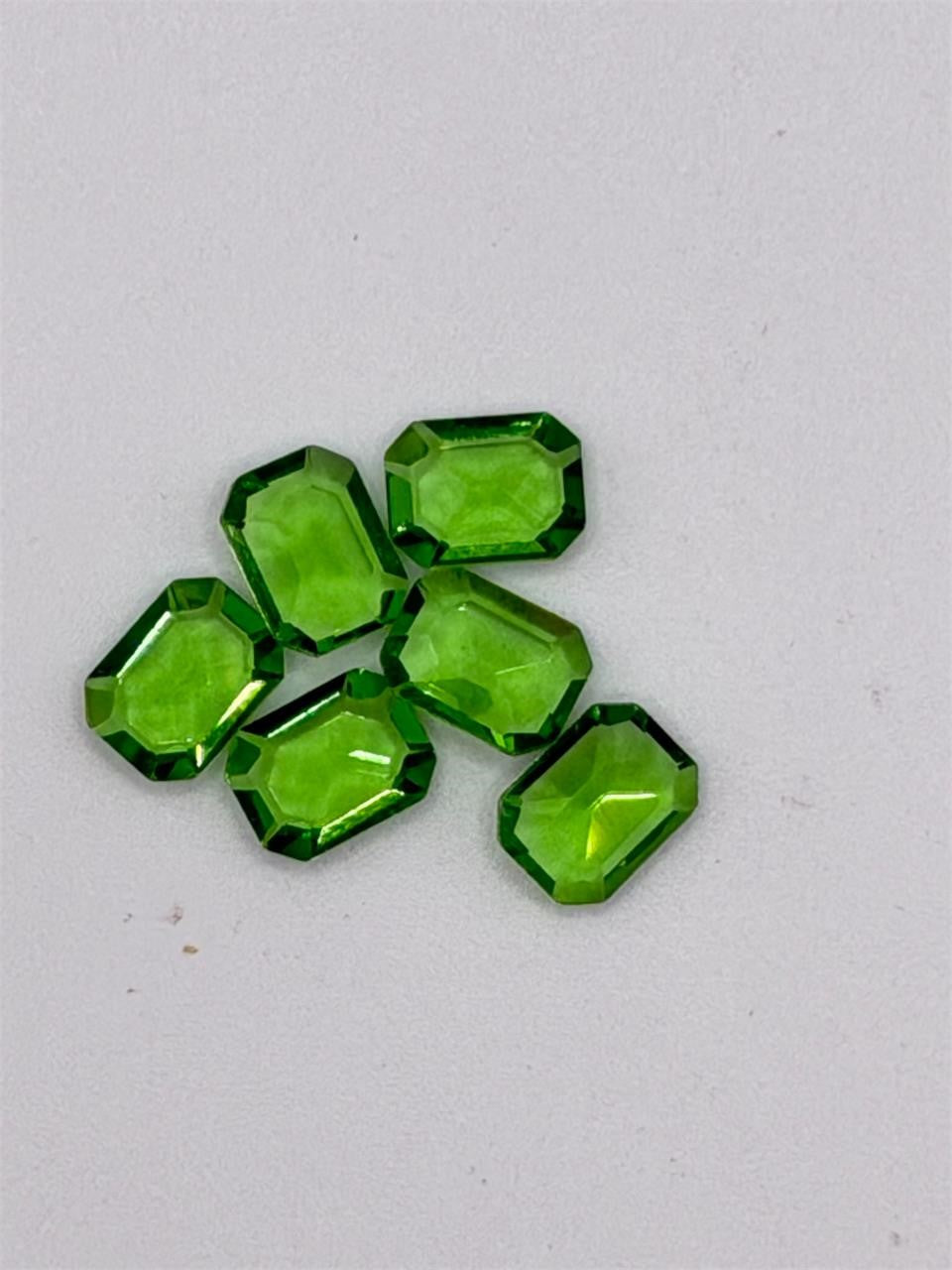 Six green emerald cut gemstones, 5x7mm, from Republic Mercantile, showcasing their vibrant color and rectangular shape.